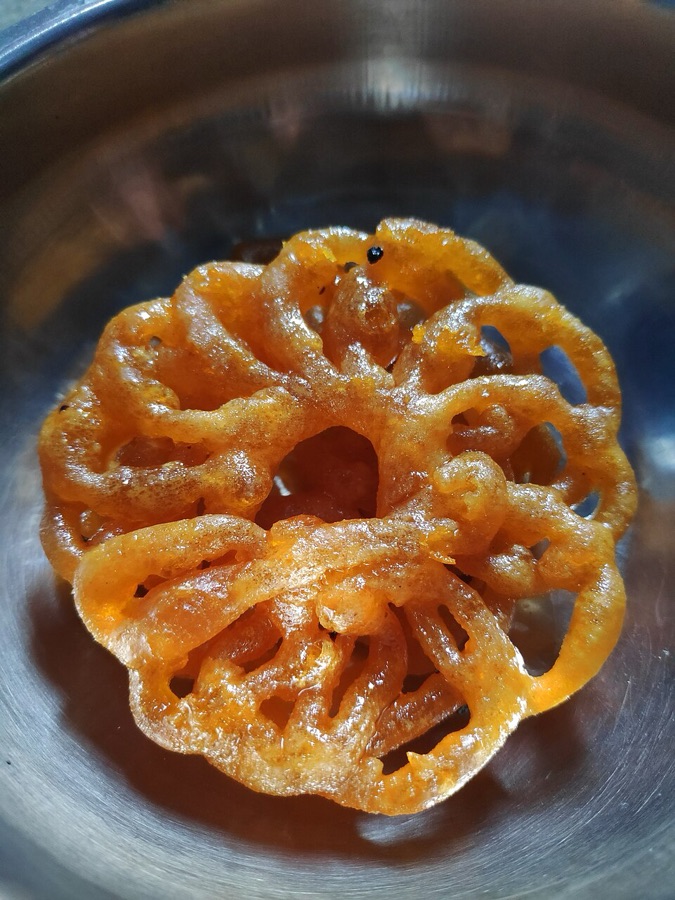A single round jalebi spiral glistening with syrup on a steel plate