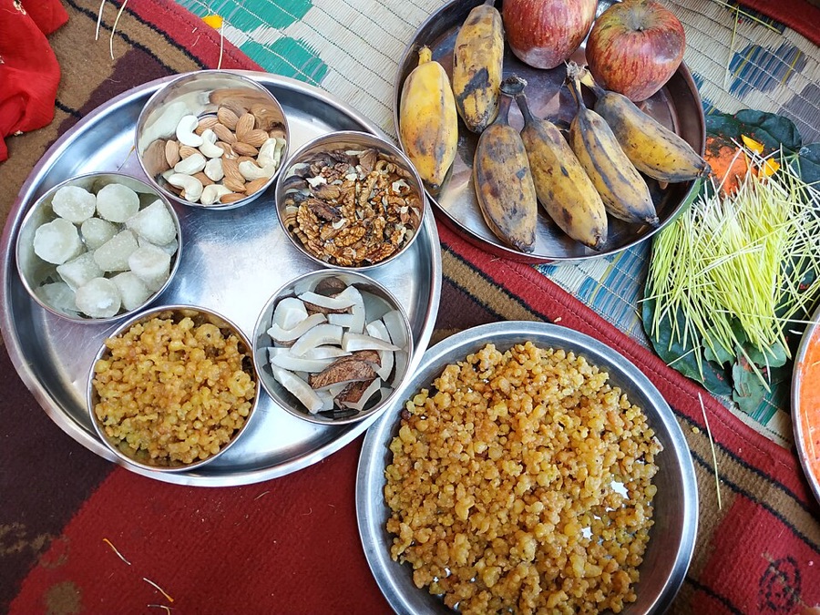 Steel plates of festival sweets, nuts, bananas and fruit laid out with jamara sprouts